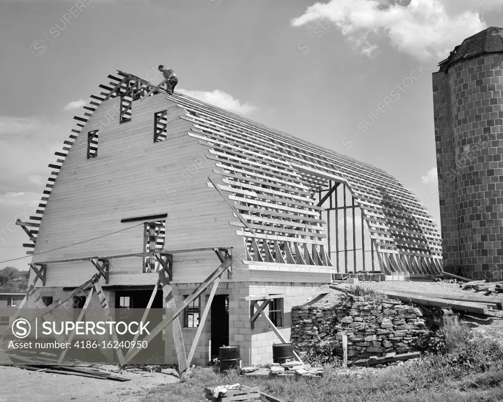 1960s MAN ON ROOF OF LARGE ROUND ROOF BARN UNDER CONSTRUCTION LITITZ PA USA