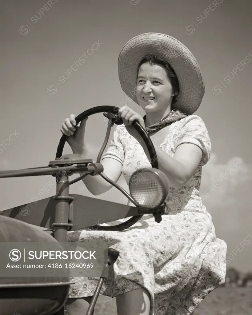 1950s 1940s SMILING WOMAN FARM WIFE WEARING DRESS STRAW HAT DRIVING A TRACTOR