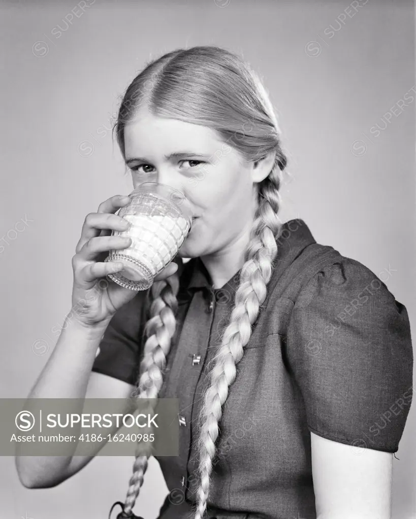 1940s BLONDE GIRL WITH LONG HAIR BRAIDS LOOKING AT CAMERA DRINKING A GLASS OF MILK