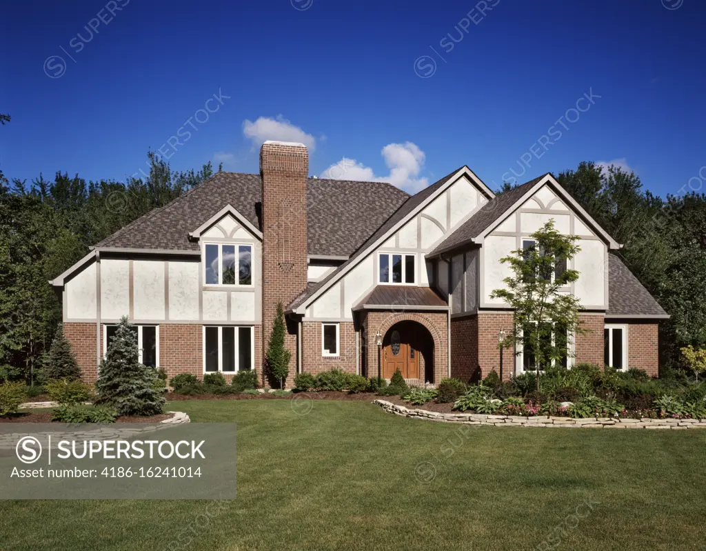 1990s SPACIOUS BRICK TWO STORY TUDOR STYLE HOUSE WITH ARCHED FRONT ENTRANCE TALL CHIMNEY AND NEW MOWN LAWN