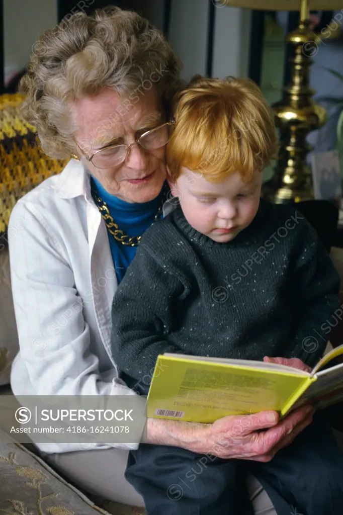 1990s RED HAIRED LITTLE BOY READING CHILDRENS BOOK SITTING ON GRANDMOTHERS LAP 