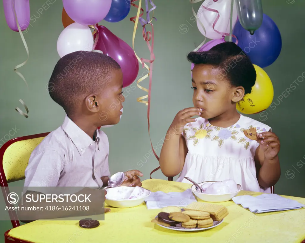 1960s AFRICAN-AMERICAN BOY AND GIRL SHARING EATING ICE CREAM AND COOKIES TOGETHER AT BIRTHDAY PARTY 