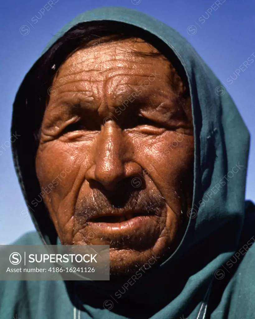 1980s CLOSE-UP PORTRAIT NATIVE AMERICAN INUIT MAN ESKIMO WEARING HOOD OVER HEAD WORN WEATHERED FACIAL FEATURES LOOKING AT CAMERA