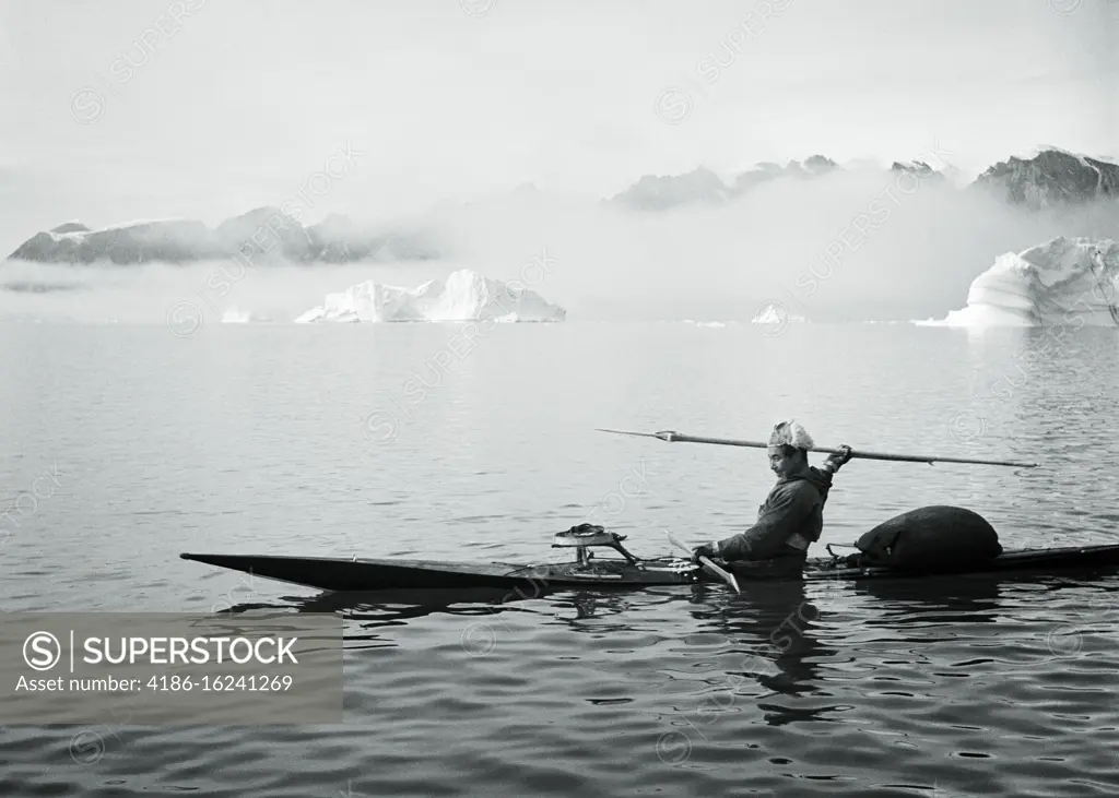 1950s MAN GREENLANDIC INUIT HUNTING HARPOONER IN KAYAK AT SYDKAP IN EASTERN GREENLAND PART OF THE SCORESBY SUND FJORD SYSTEM