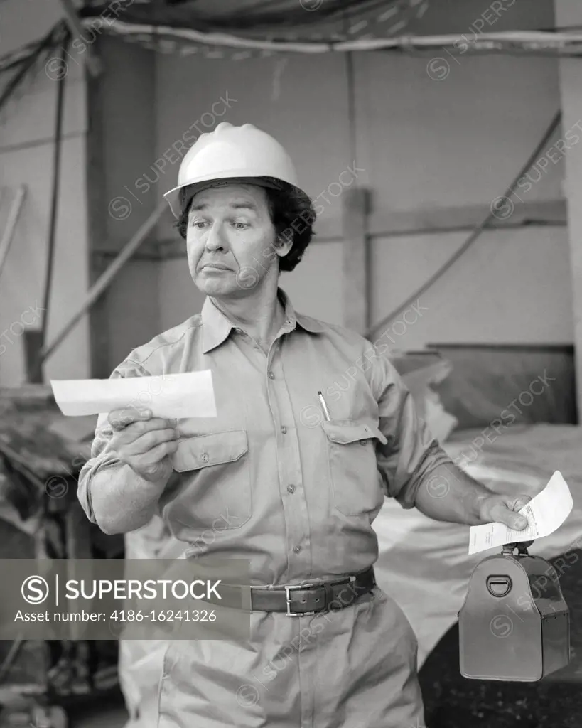 1970s SURPRISED WORKMAN WEARING WORK CLOTHES HARD HAT CARRYING LUNCH BOX  HOLDING PAYCHECK WITH SATISFIED FACIAL EXPRESSION - SuperStock