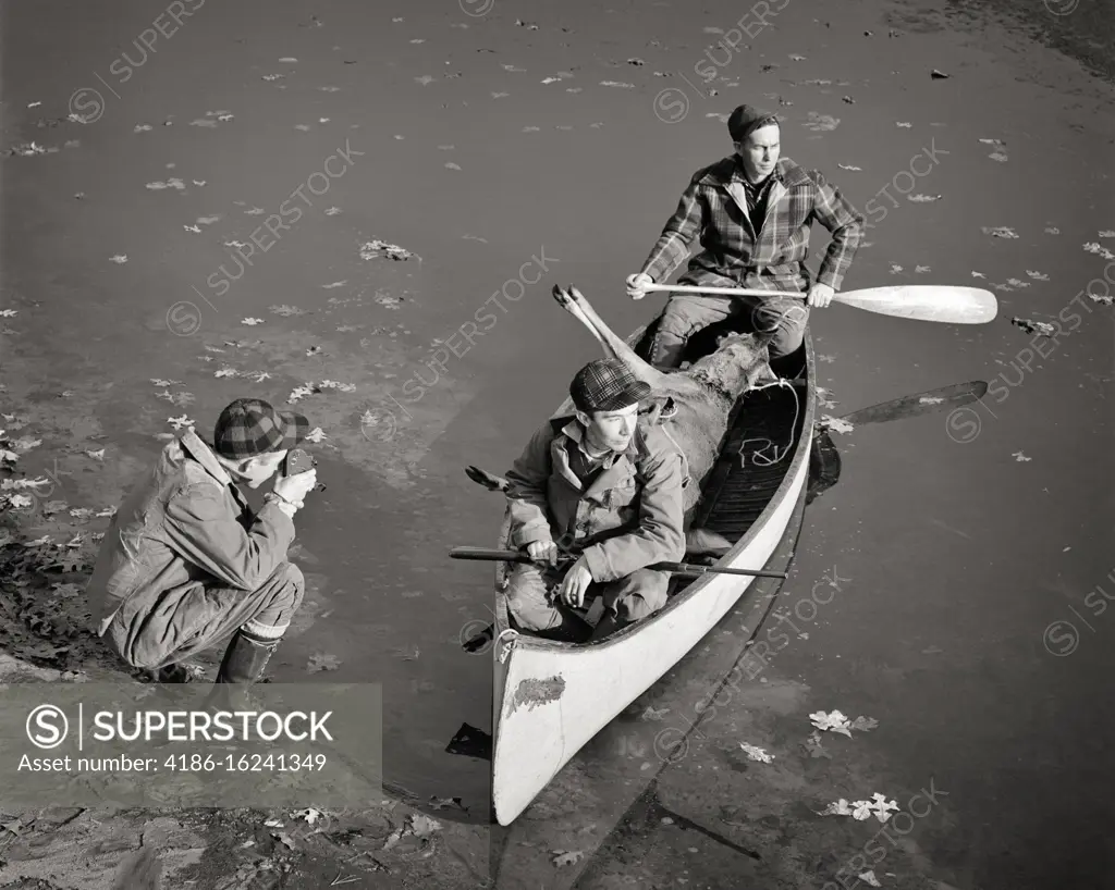 1940s SPORTS MOVIE PHOTOGRAPHER FILMING FOOTAGE OF TWO HUNTERS WITH HARVESTED DEER IN CANOE ONE MAN PADDLING SECOND WITH RIFLE