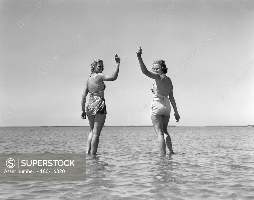 1930S Two Girls Standing In Water Wearing Bathing Suits Looking Back Waving