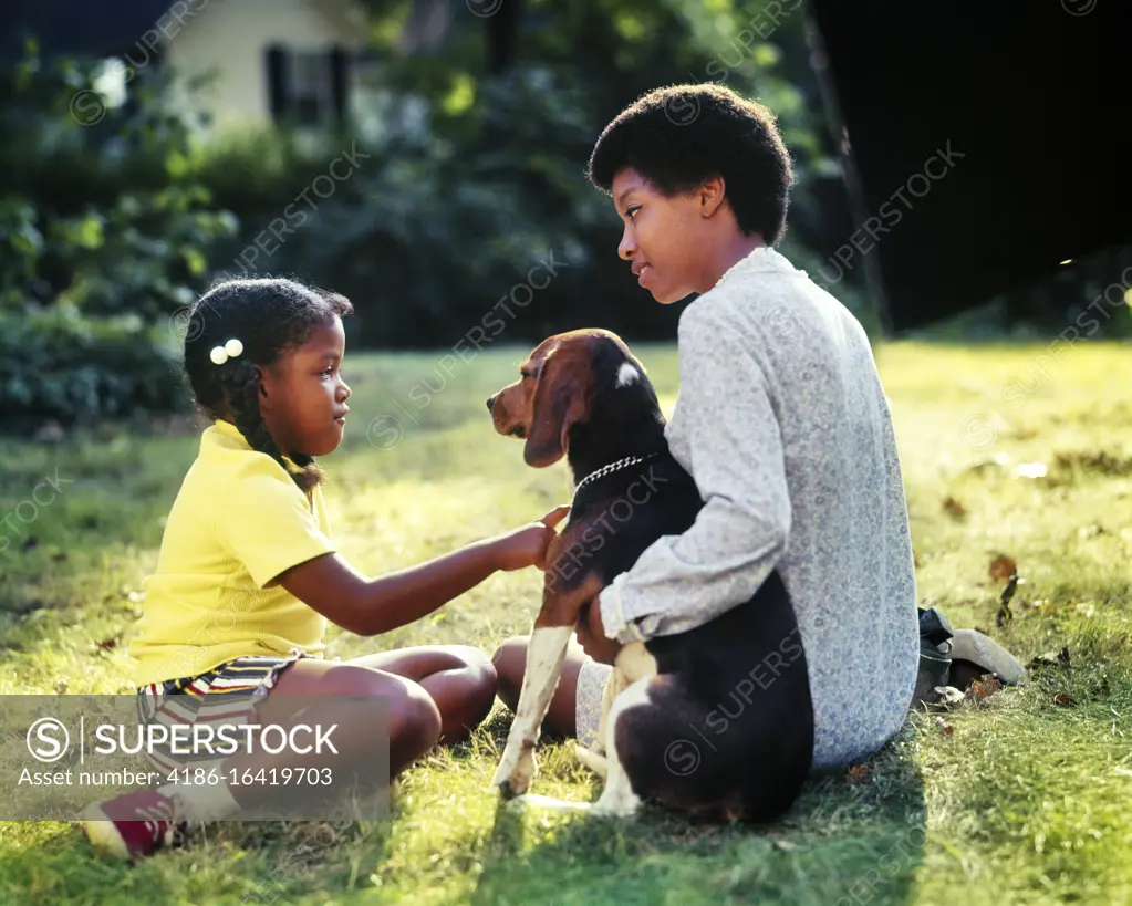 1970s 1980s SERIOUS AFRICAN-AMERICAN MOTHER TEACHING INSTRUCTING DAUGHTER ABOUT CARING FOR PET HOUND DOG WHILE SITTING IN YARD