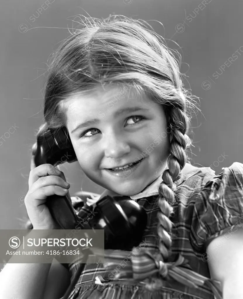 1930S 1940S Portrait Of Smiling Little Girl With Long Pigtails Talking On Telephone