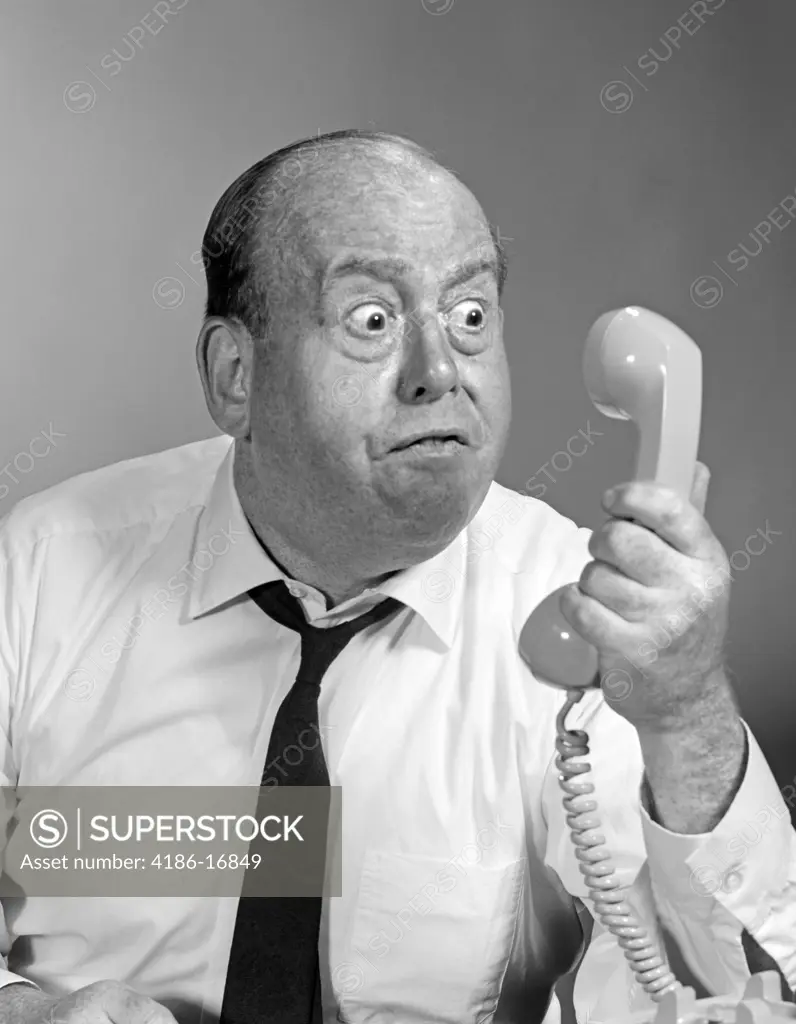 1960S 1970S Angry Balding Man Looking Bug-Eyed Into Telephone Receiver