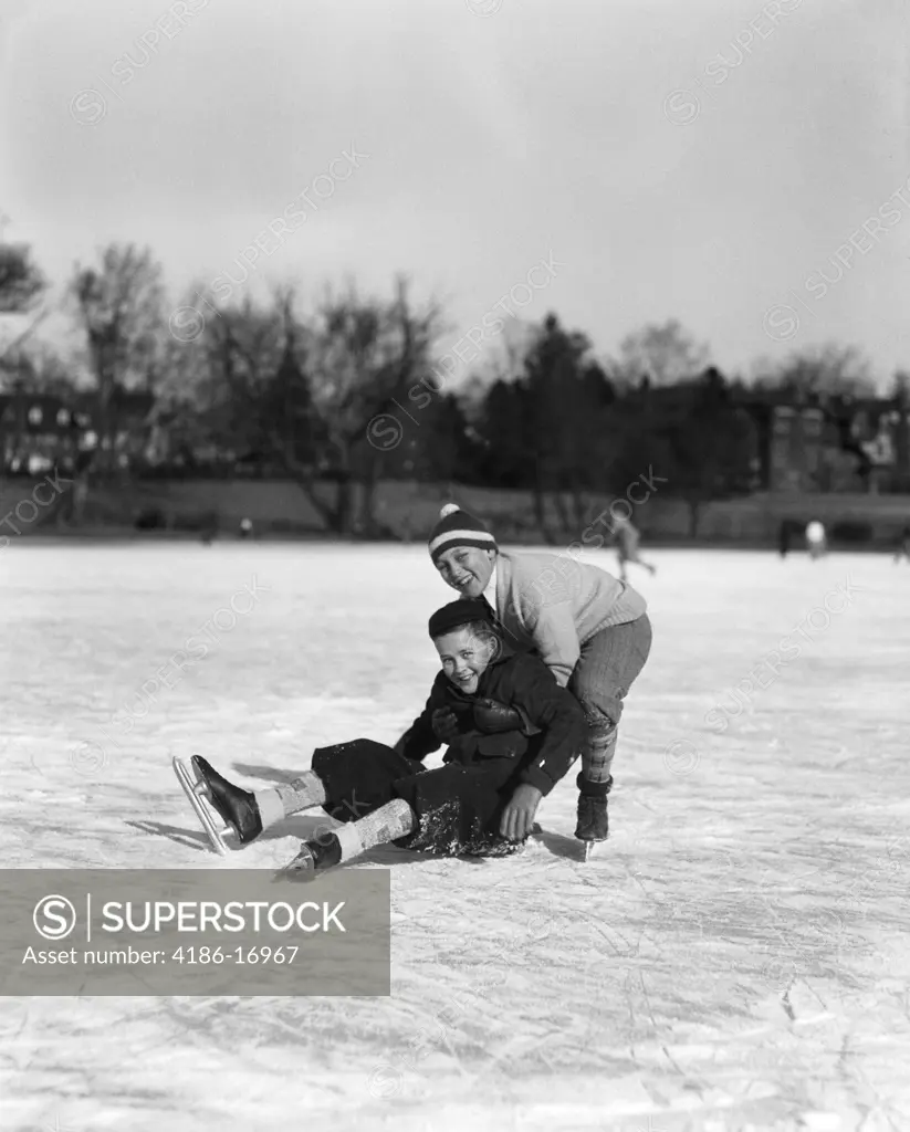 1920S 1930S Two Smiling Boys Ice Skating One Boy Fallen Other Picking Him Up