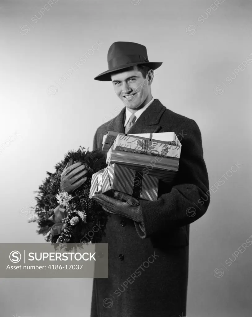 1950S Smiling Young Man In Hat Coat And Gloves Holding Christmas Wreath And Wrapped Gifts