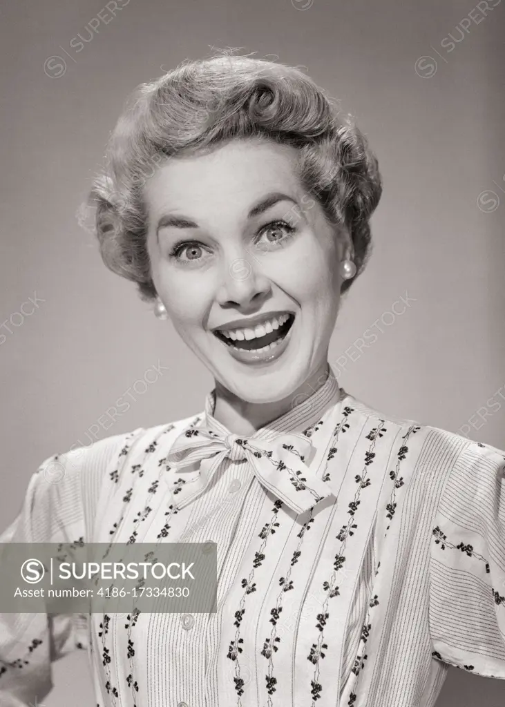 1950s PORTRAIT OF BLOND WOMAN EYES WIDE OPEN BIG SMILE WEARING PRINT STRIPE BLOUSE THAT TIES AT THE NECK LOOKING AT CAMERA