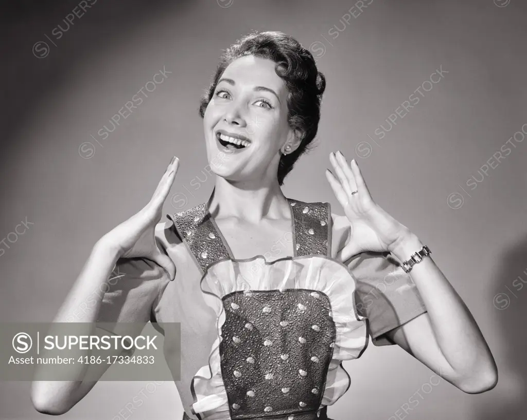 1950s PROUD BRUNETTE HOUSEWIFE SMILING WEARING APRON MAKING GESTURE OF THUMBS TUCKED LOOKING AT CAMERA