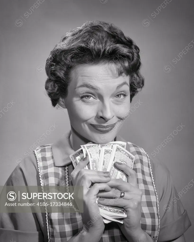 1950s SMILING BRUNETTE WOMAN HOUSEWIFE LOOKING AT CAMERA HOLDING BUNDLE OF MONEY CASH BILLS DISCOUNTS SAVINGS WINNINGS FORTUNE