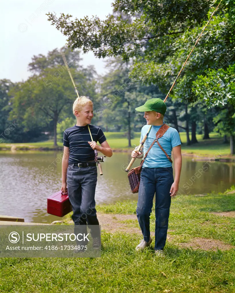 1970s TWO BOYS WALKING ALONG LAKESIDE TALKING CARRYING FISHING