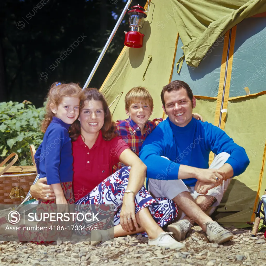 1970s PORTRAIT OF SMILING FAMILY OF FOUR MOTHER FATHER SON DAUGHTER LOOKING AT CAMERA POSED OUTSIDE THEIR CAMPSITE TENT 