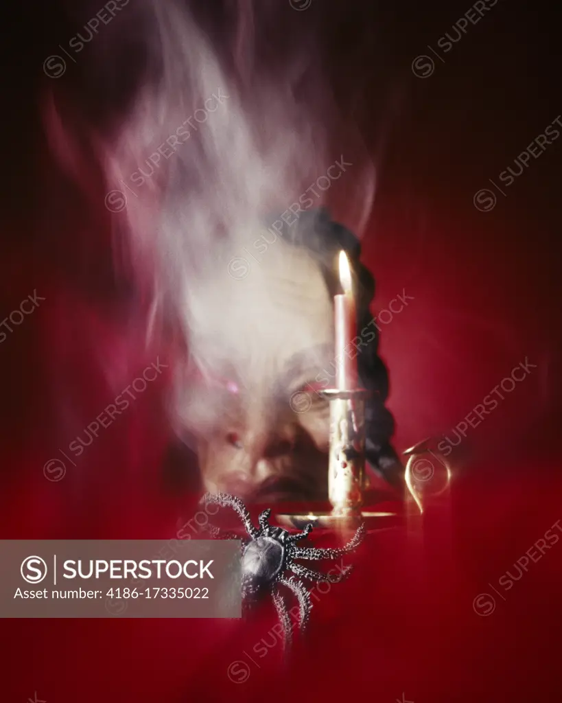 1970s SPOOKY STILL LIFE SCORPION LIKE BLACK SPIDER BURNING CANDLE GROTESQUE HUMAN FACE WITH RED EYES IN SMOKEY RED WHITE MIST