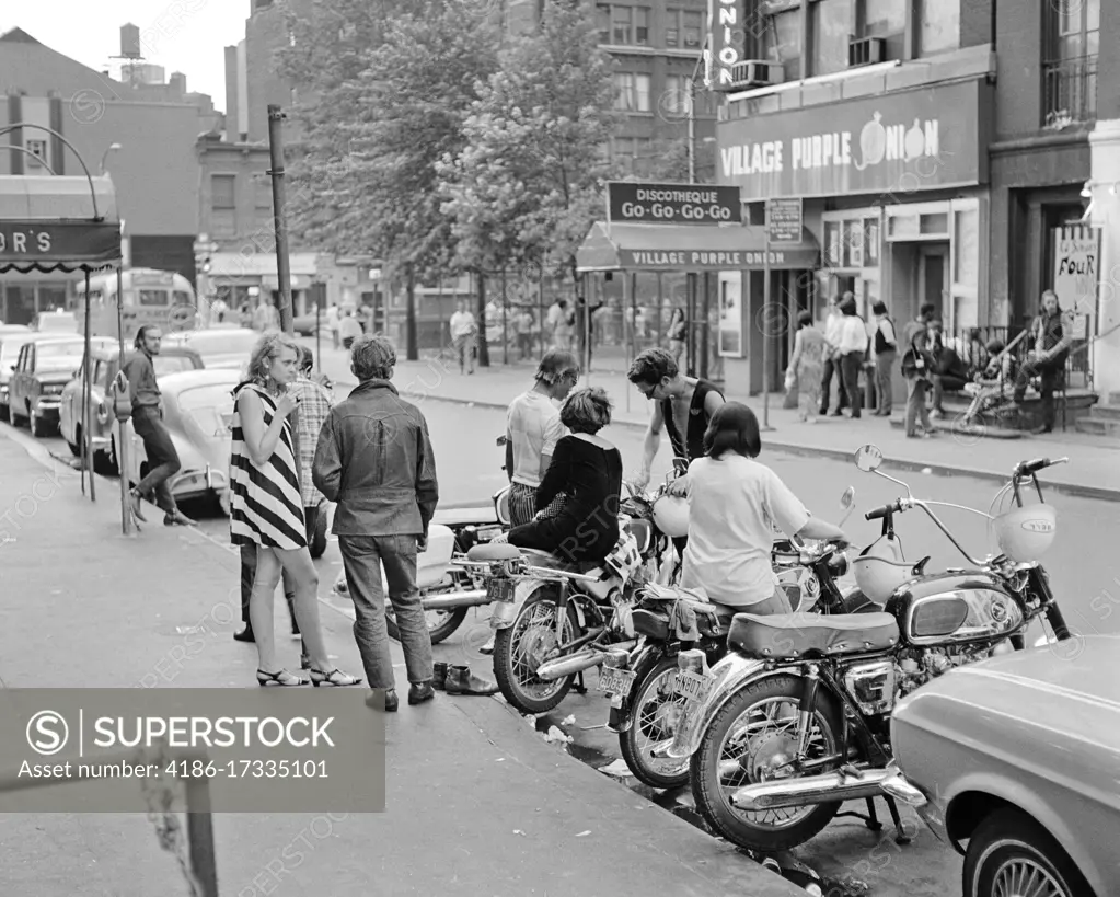 1960s GREENWICH VILLAGE STREET SCENE GROUP OF YOUNG ADULTS BY MOTOR BIKES ACROSS STREET FROM THE PURPLE ONION A FAMOUS GO-GO BAR