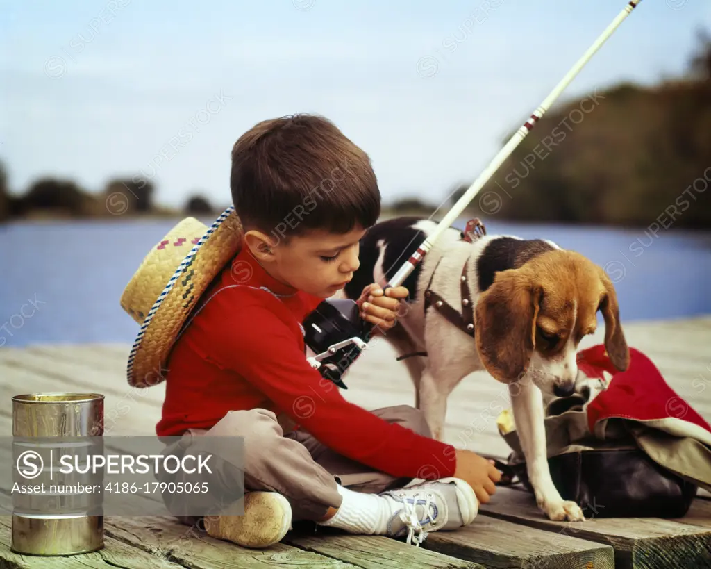 1950s 1960s YOUNG BOY WEARING RED SHIRT STRAW HAT TOGETHER WITH PET BEAGLE DOG SITTING BY BIG TIN CAN OF BAIT FISHING OFF DOCK