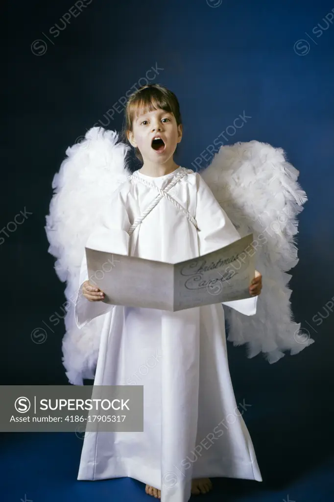 1960s CUTE LITTLE GIRL IN WHITE ANGEL GOWN COSTUME WITH WINGS LOOKING AT CAMERA SINGING CHRISTMAS CAROLS IN SUNDAY SCHOOL PLAY