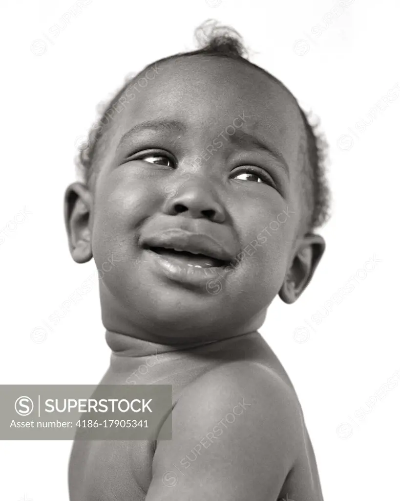 1940s SMILING AFRICAN AMERICAN BABY BOY LOOKING UP AND BACK OVER HIS SHOULDER