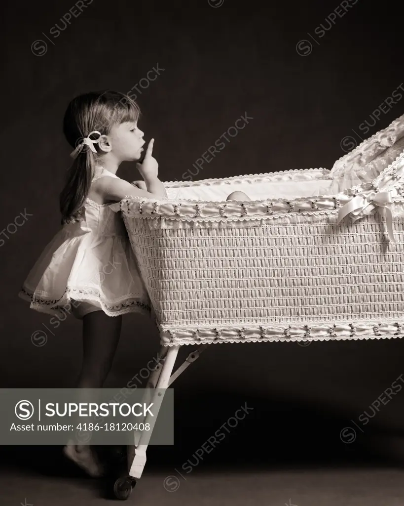 1970s LITTLE GIRL ON TIPTOE LOOKING INTO BABY BASSINET CRIB MAKING SHUSHING GESTURE WITH FINGER TO HER LIPS