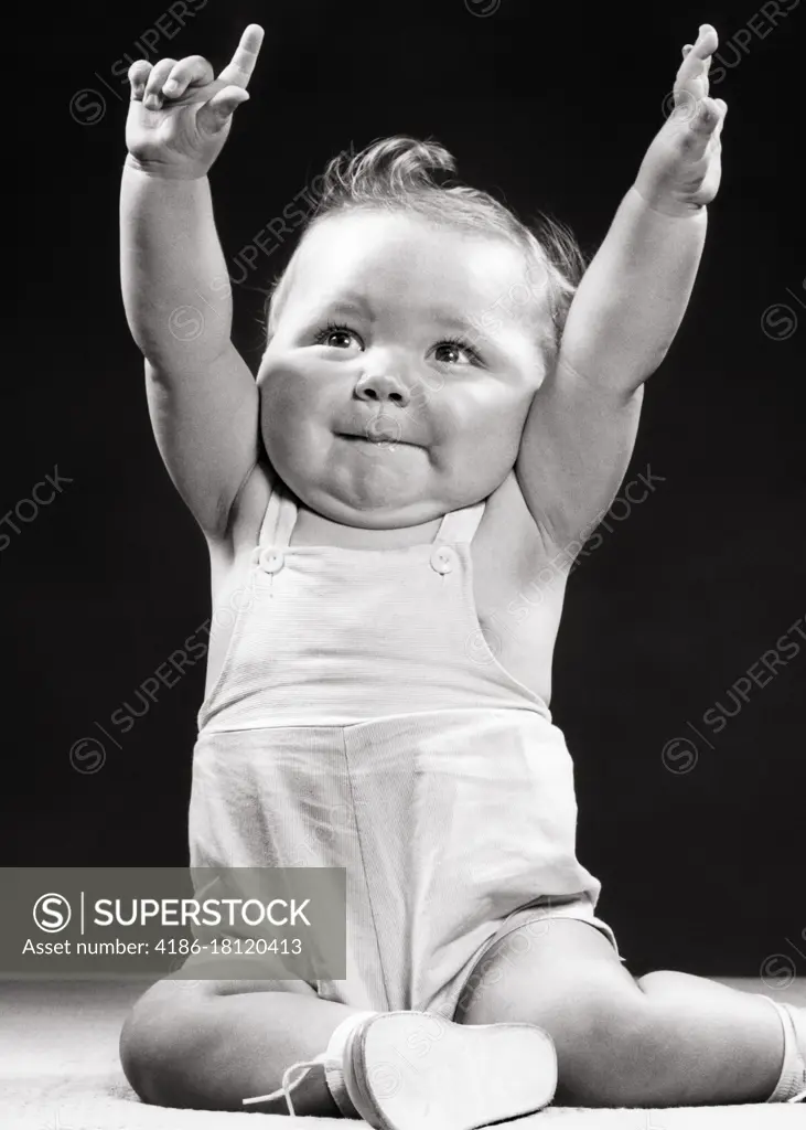 1950s BABY BOY TODDLER SITTING WITH ARMS RAISED HANDS UP ONE HAND MAKING ENTHUSIASTIC NUMBER ONE SIGN