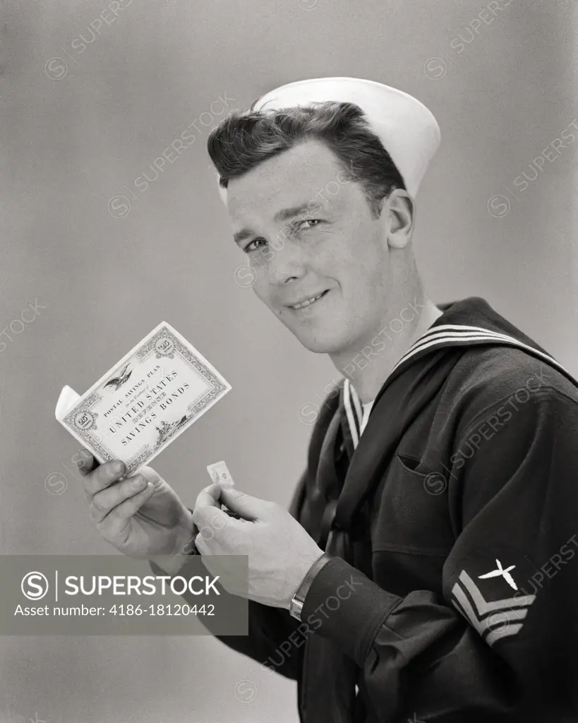 1940s SMILING NAVY SAILOR LOOKING AT CAMERA HOLDING WORLD WAR 2 UNITED STATES SAVINGS BOND POSTAL PLAN BOOKLET AND STAMP 