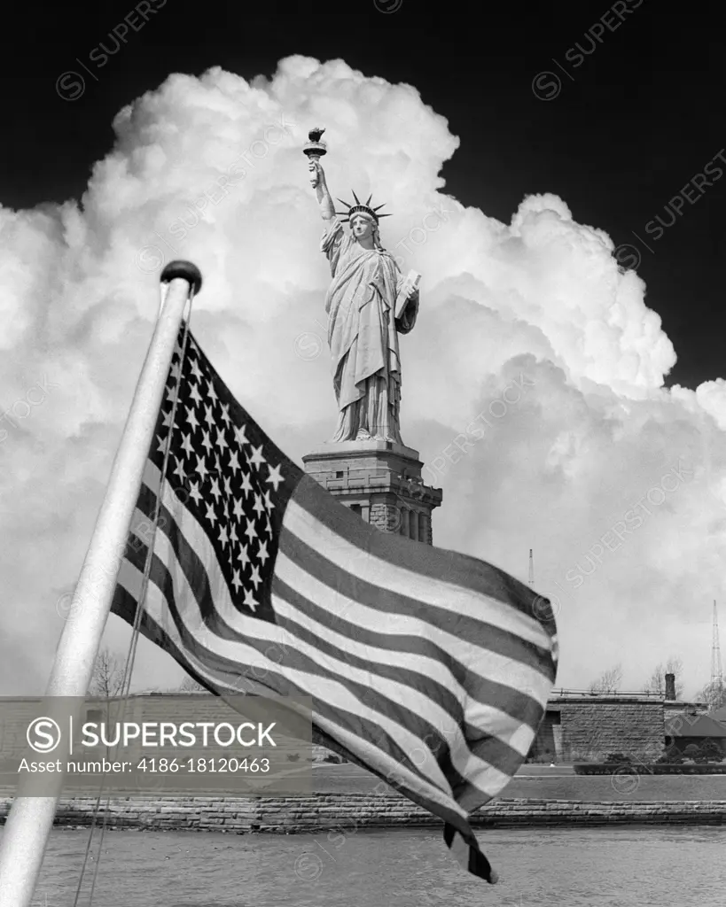 1940s COMPOSITE IMAGE OF STATUE OF LIBERTY WITH DRAMATIC CLOUD BEHIND AND 48 STAR AMERICAN FLAG OVERLAY IN FOREGROUND