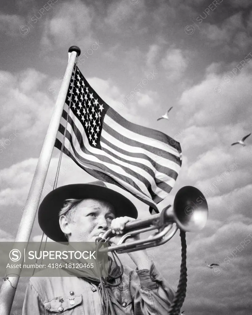 1930s 1940s BOY SCOUT IN UNIFORM BLOWING A BUGLE IN FRONT OF A 48 STAR AMERICAN FLAG 