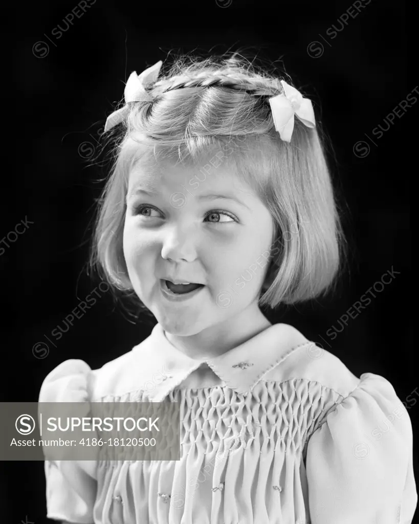 1940s SMILING CUTE BLOND GIRL LOOKING OFF TO SIDE WITH MISCHIEF IN EYES BOWS AND BRAID IN HAIR AND SMOCKING ON DRESS 