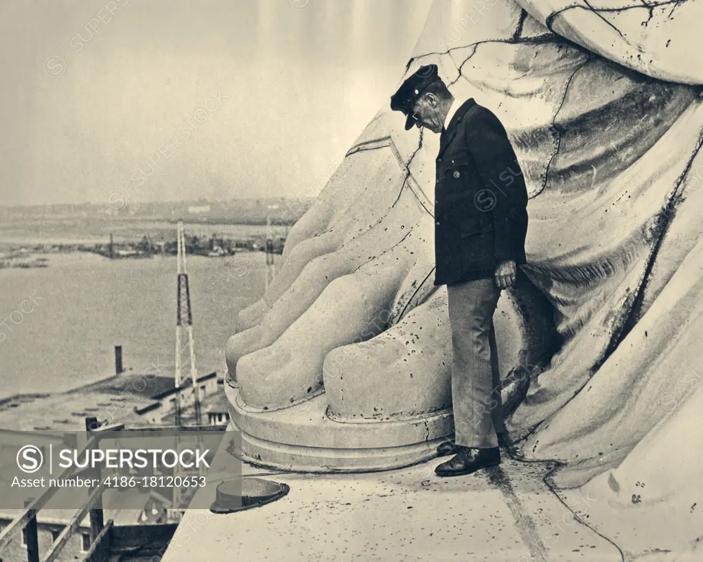 1920s 1930s MAN STANDING BY BIG TOE OF COPPER FOOT OF THE STATUE OF LIBERTY NEW YORK HARBOR USA