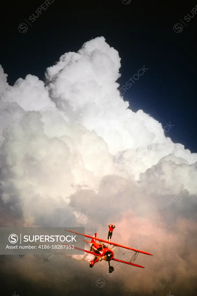 1990s ANONYMOUS MAN A DAREDEVIL WING WALKER PERFORMING ATOP A BIPLANE FLYING THROUGH DRAMATIC CUMULUS CLOUDS 