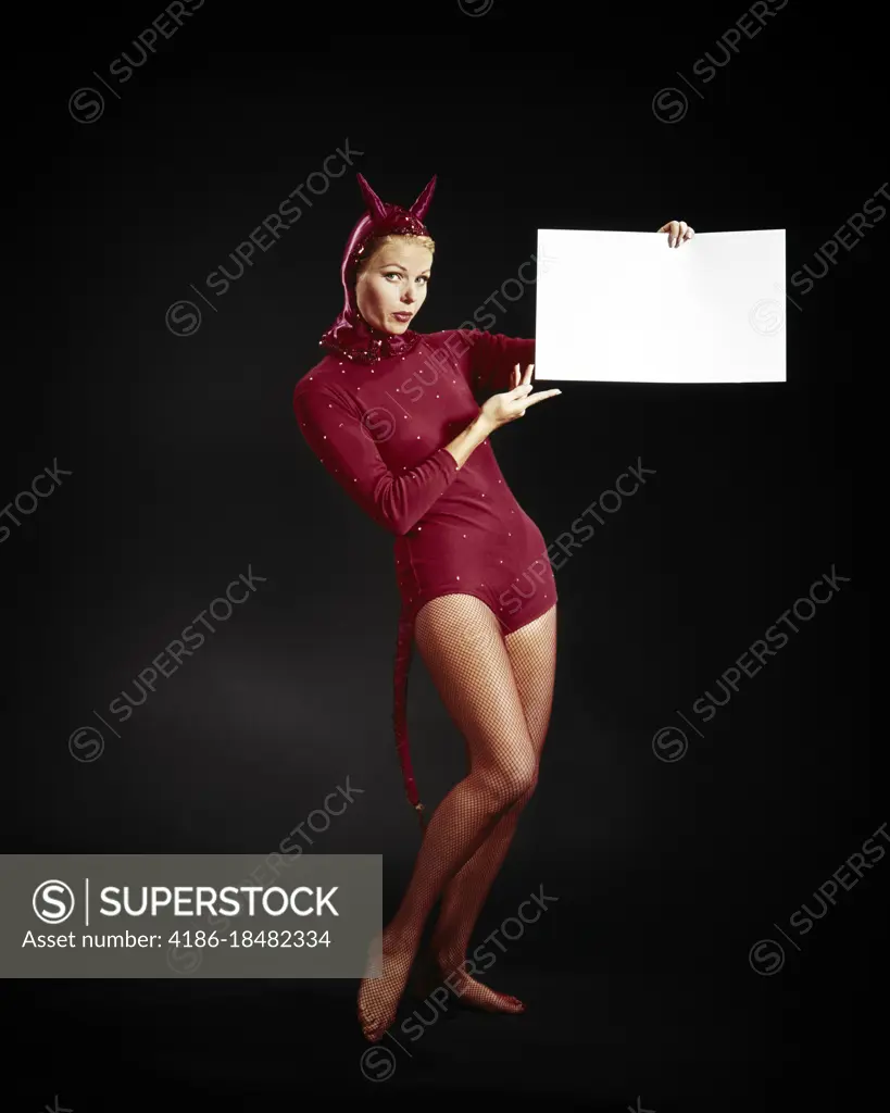 1960s BLONDE WOMAN DRESSED AS THE DEVIL IN RED LEOTARD COSTUME LOOKING AT THE CAMERA HOLDING A BLANK SIGN