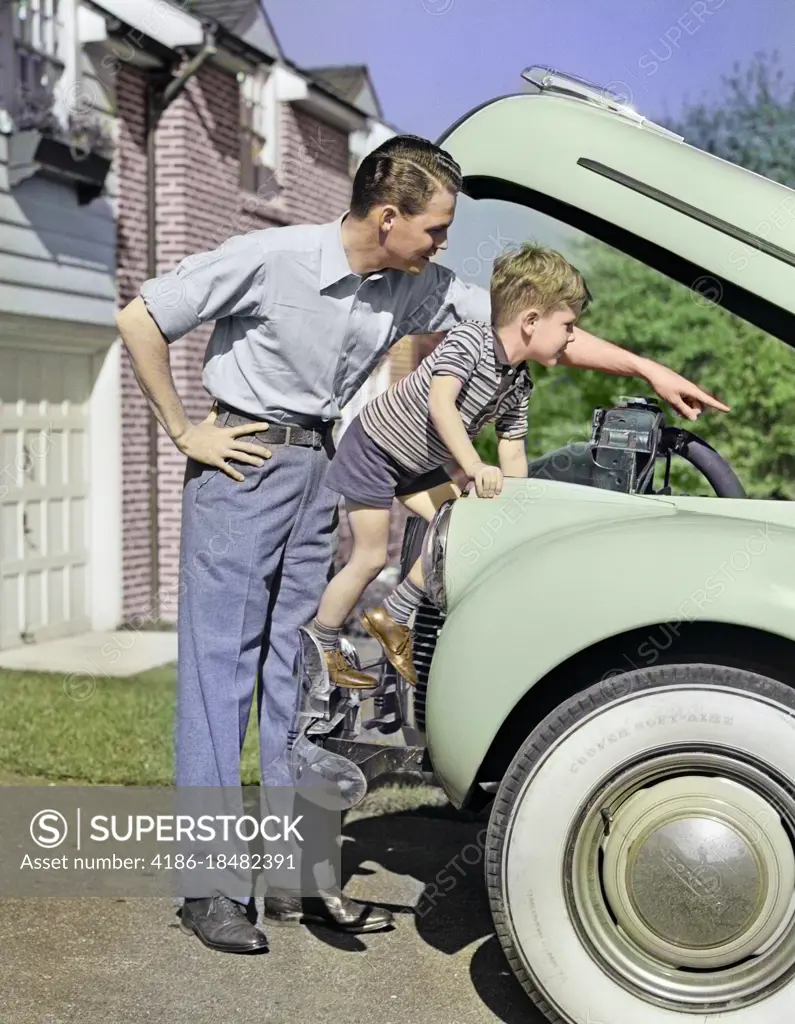 1940s MAN FATHER AND BOY SON CHECKING UNDER HOOD OF CAR IN DRIVEWAY IN FRONT OF SUBURBAN HOUSE