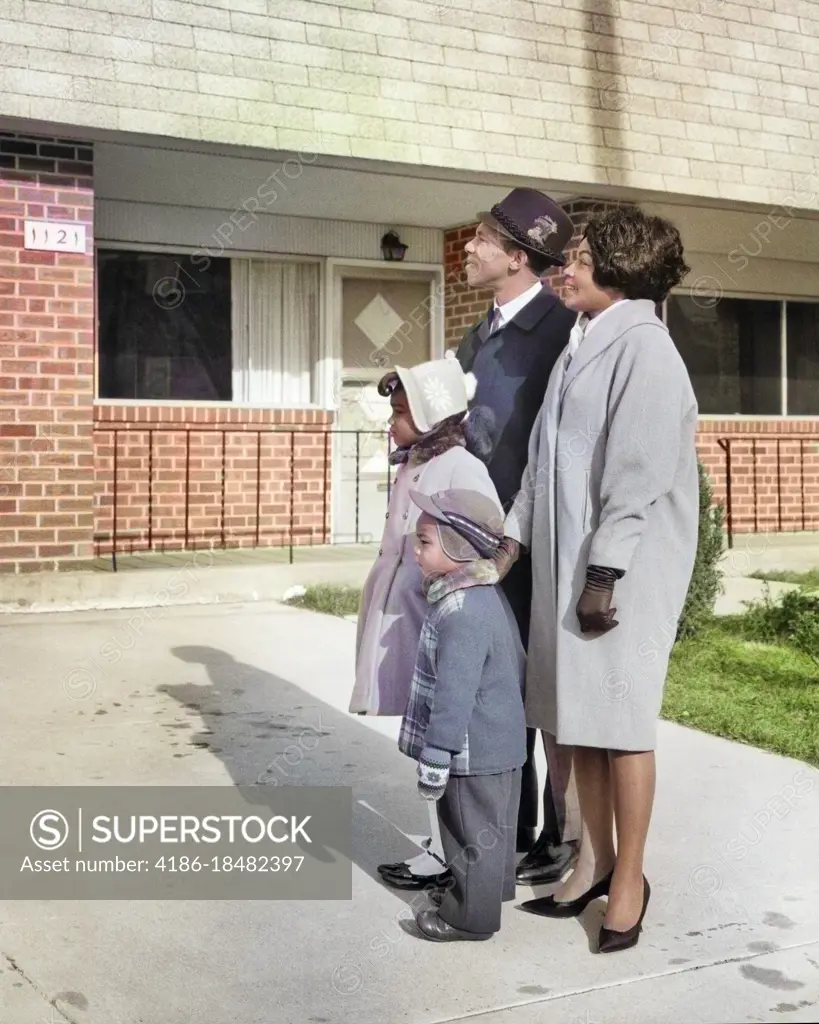 1960s SMILING AFRICAN-AMERICAN FAMILY STANDING IN THE DRIVEWAY OF NEW HOUSE WEARING HATS COATS GLOVES