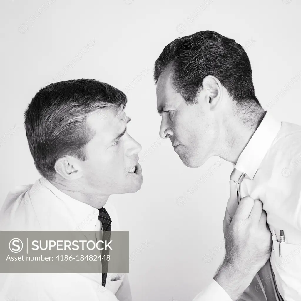 1960s TWO ANGRY ARGUING YELLING BUSINESSMEN HEAD TO HEAD HAND GRABBING SHIRT ENRAGED FURIOUS FACIAL EXPRESSIONS