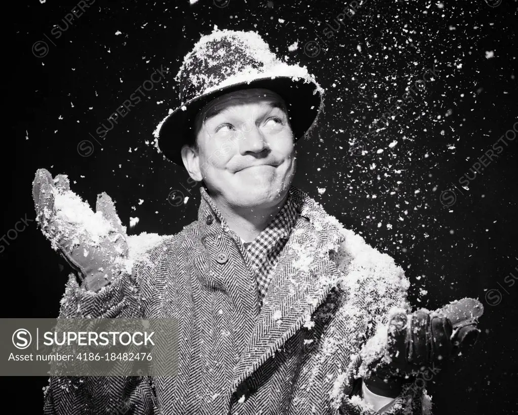 1950s SNOW FALLING AT NIGHT ON SMILING MAN BUNDLED UP FOR WINTER IN HAT SCARF OVERCOAT AND GLOVES HANDS MAKING ACCEPTING GESTURE