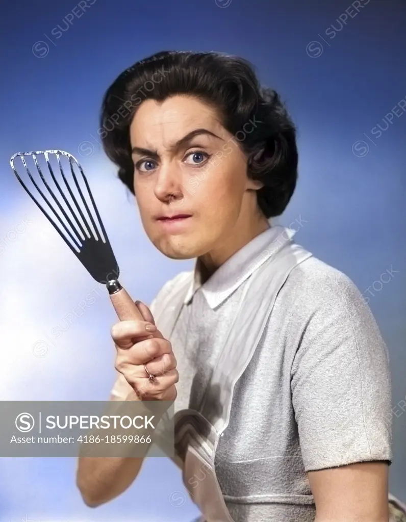 1950s 1960s PORTRAIT OF ANGRY WOMAN HOUSEWIFE LOOKING AT CAMERA BRANDISHING FOOD TURNER KITCHEN SPATULA