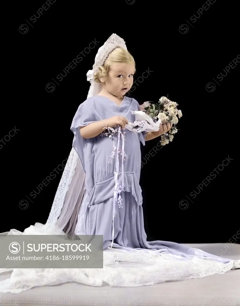 1940s LITTLE BLOND GIRL IN OVERSIZED WEDDING GOWN & VEIL HOLDING BOUQUET WITH CONFUSED EXPRESSION LOOKING AT CAMERA