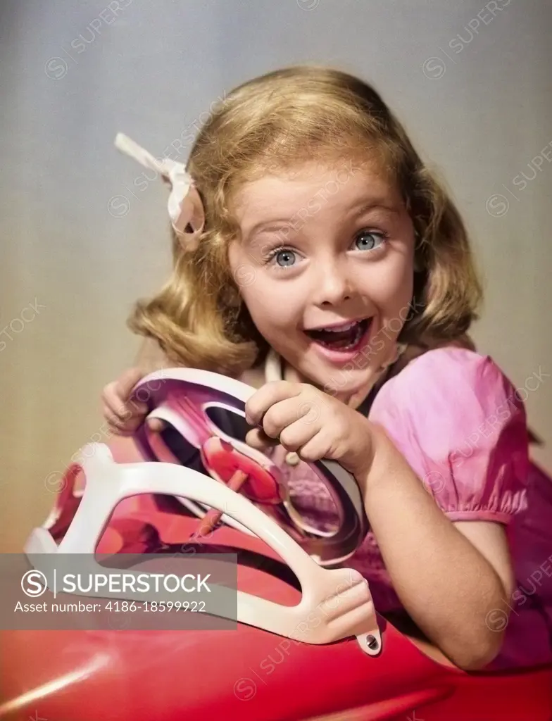 1950s PORTRAIT OF LITTLE GIRL DRIVING TOY CAR WITH EXCITED EXPRESSION LOOKING AT CAMERA