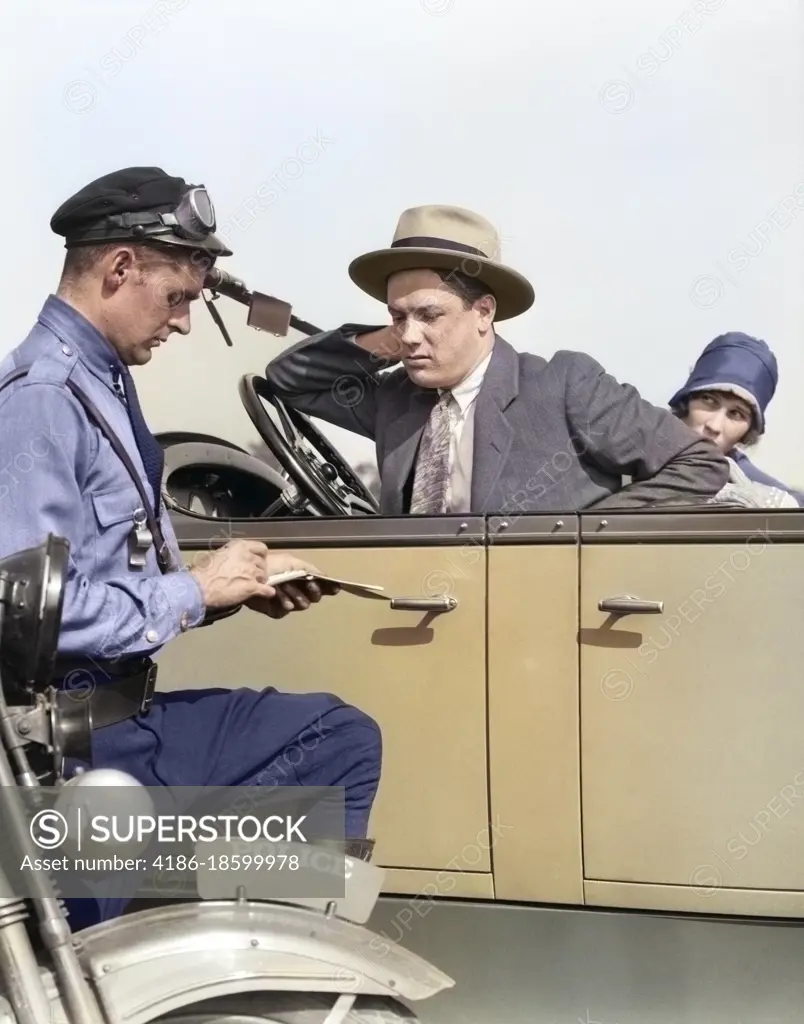 1920s MOTORCYCLE POLICEMAN WRITING A SPEEDING TICKET TO A COUPLE SITTING IN CONVERTIBLE FOUR-DOOR SEDAN AUTOMOBILE