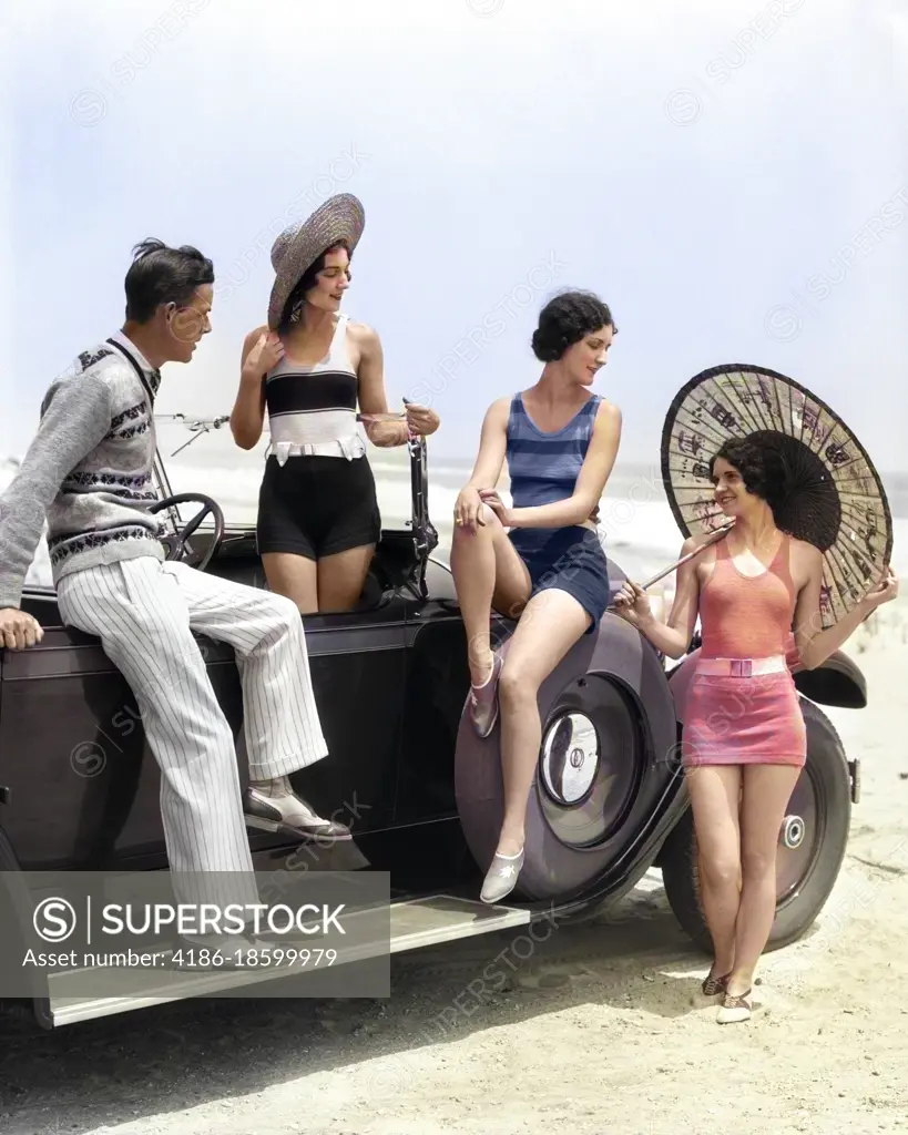 1920s MAN AND THREE WOMEN IN BEACH CLOTHES OR BATHING SUITS POSING AROUND CAR ON RUNNING BOARD AT SEASHORE