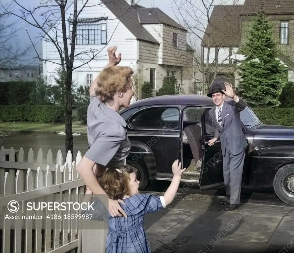 1940s 1950s MOTHER AND DAUGHTER WAVING TO FATHER OPENING AUTOMOBILE DOOR IN FRONT OF SUBURBAN HOME