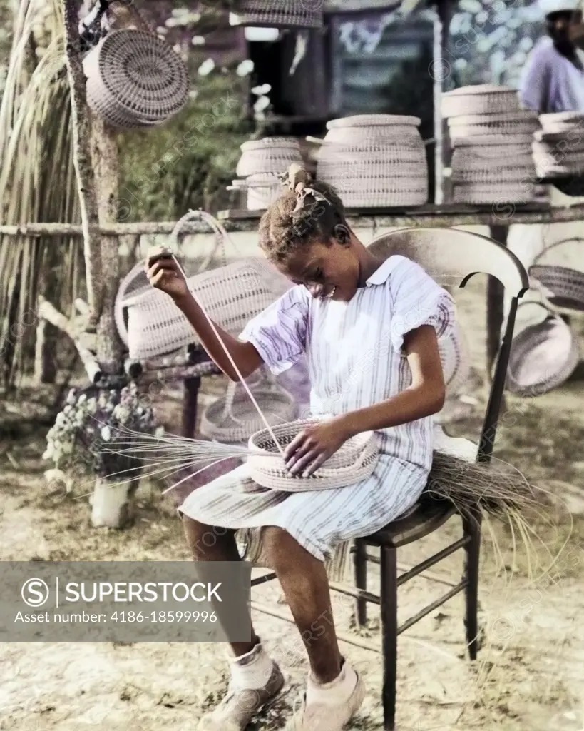 1930s 1940s ANONYMOUS SMILING YOUNG AFRICAN-AMERICAN GULLAH GIRL WEAVING MAKING BASKET FROM SWEETGRASS SOUTH CAROLINA USA