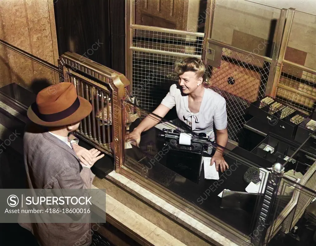 1940s SMILING WOMAN BANK TELLER BEHIND CAGE SERVING MALE CUSTOMER