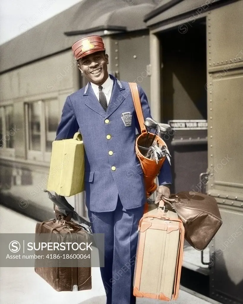 1930s SMILING AFRICAN-AMERICAN MAN RED CAP PORTER CARRYING LUGGAGE IN TRAIN STATION 