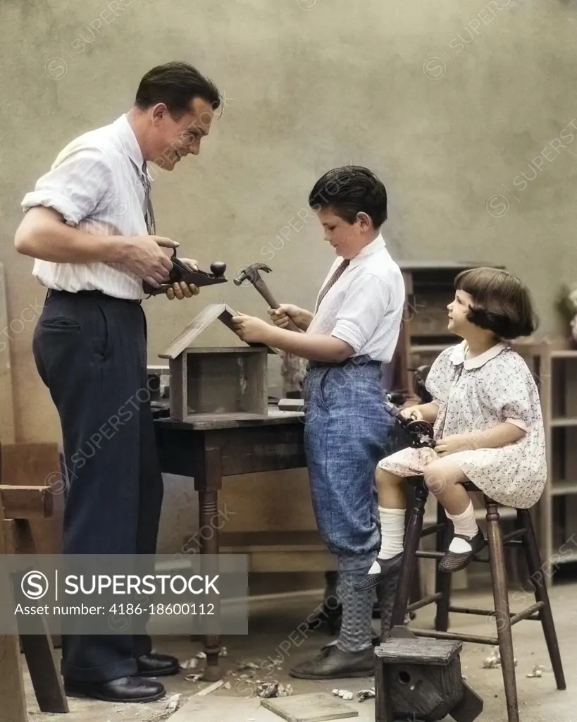 1920s FAMILY FATHER CARPENTER TEACHING SON AND DAUGHTER TO BUILD A BIRDHOUSE WITH WOODWORKING TOOLSI