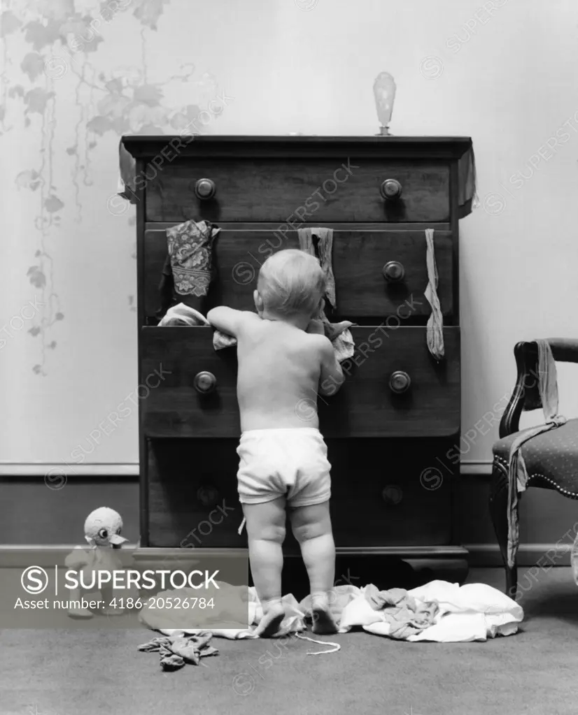 1940s TODDLER BABY PULLING CLOTHES OUT OF BUREAU DRAWERS MAKING A MESS